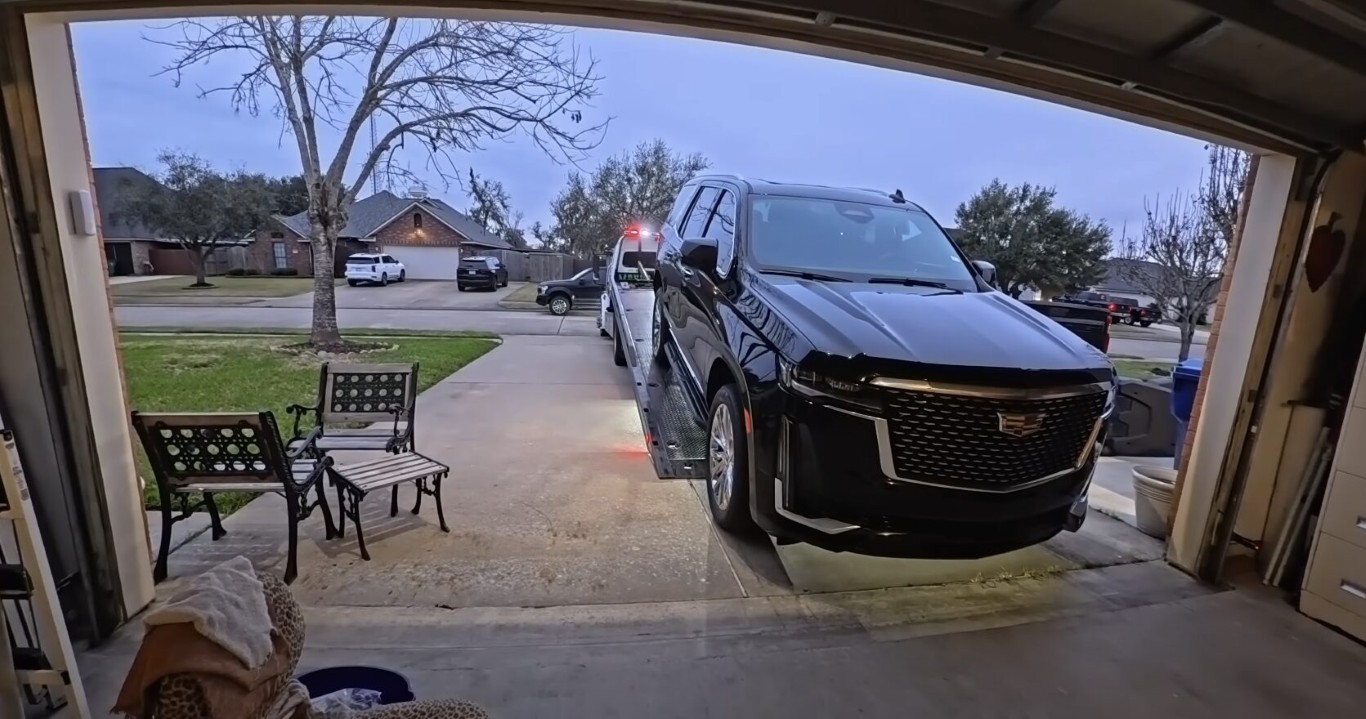 Tow truck operator assisting with a black Cadillac SUV from a residential driveway in Amityville, NY