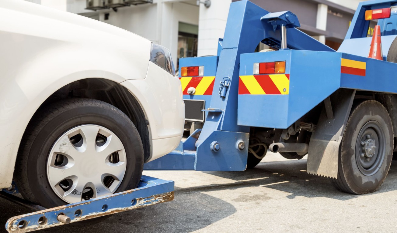 Blue wheel-lift tow truck securing a white car for battery service and towing